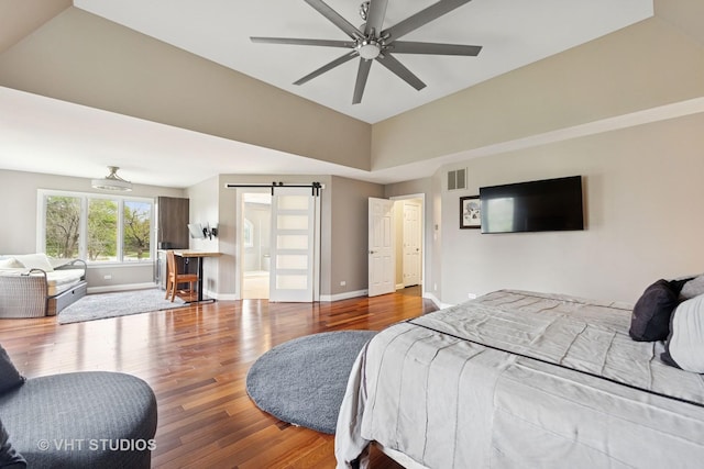 bedroom featuring a barn door, baseboards, wood finished floors, lofted ceiling, and visible vents