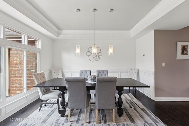 dining area featuring wainscoting, a decorative wall, a tray ceiling, and wood finished floors