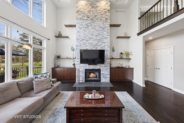 living room featuring a high ceiling, a stone fireplace, baseboards, dark wood-type flooring, and visible vents