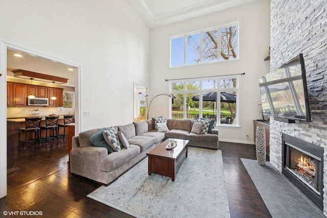 living area with a high ceiling, a stone fireplace, and dark wood-type flooring