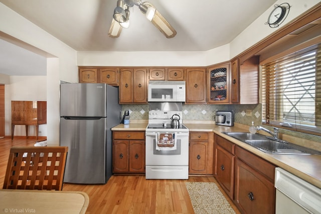 kitchen featuring brown cabinetry, light wood finished floors, a sink, and white appliances