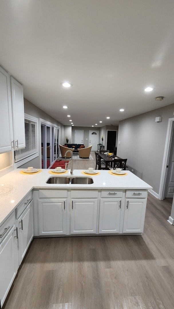 kitchen with white cabinets, recessed lighting, wood finished floors, light countertops, and a sink
