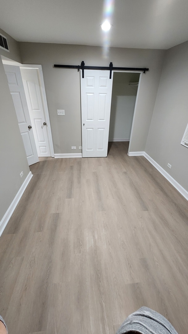 unfurnished bedroom with a barn door, visible vents, baseboards, and wood finished floors