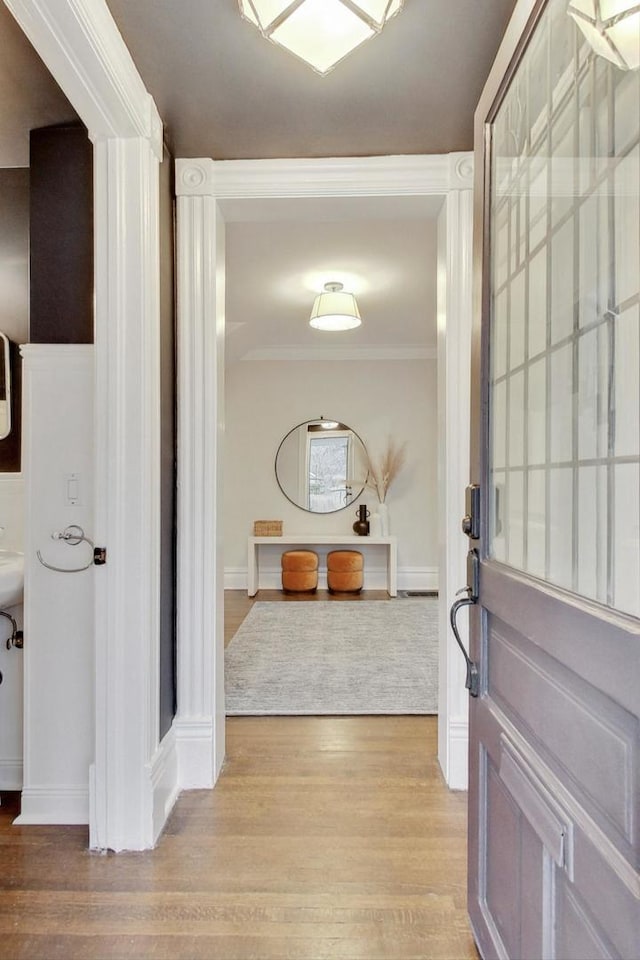 hallway with ornamental molding, light wood-style flooring, and baseboards