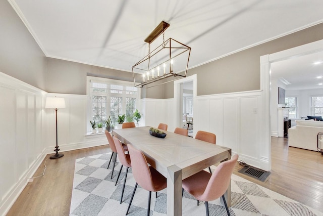 dining area featuring a decorative wall, light wood-style flooring, an inviting chandelier, and a wainscoted wall