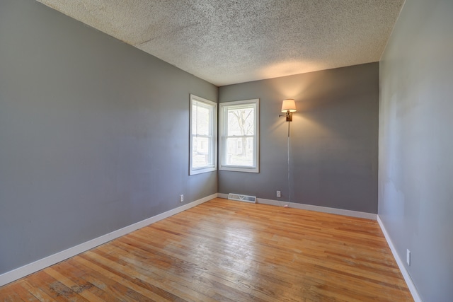spare room featuring baseboards, light wood finished floors, a textured ceiling, and visible vents