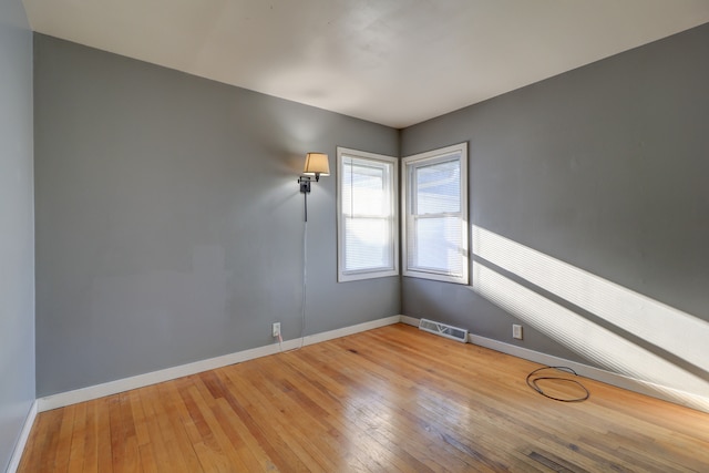 empty room featuring baseboards, hardwood / wood-style flooring, and visible vents