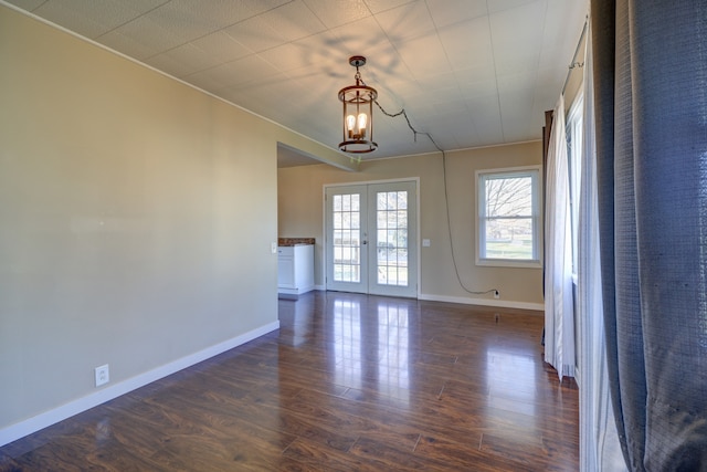 spare room with baseboards, french doors, dark wood-style floors, and an inviting chandelier