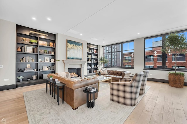 living area with wood-type flooring, recessed lighting, built in shelves, and a lit fireplace