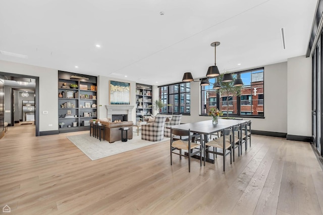 dining area with built in features, baseboards, light wood finished floors, a warm lit fireplace, and recessed lighting