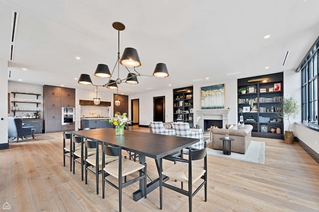 dining area featuring a warm lit fireplace, recessed lighting, built in shelves, light wood-style flooring, and a notable chandelier