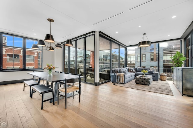 dining area with light wood-type flooring, floor to ceiling windows, a chandelier, and a healthy amount of sunlight