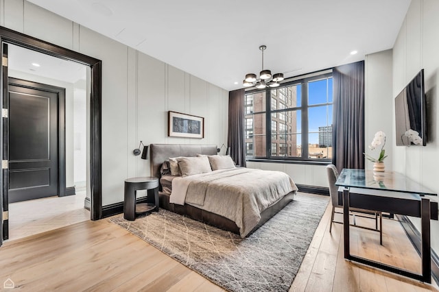bedroom featuring a decorative wall, a chandelier, and light wood-style floors