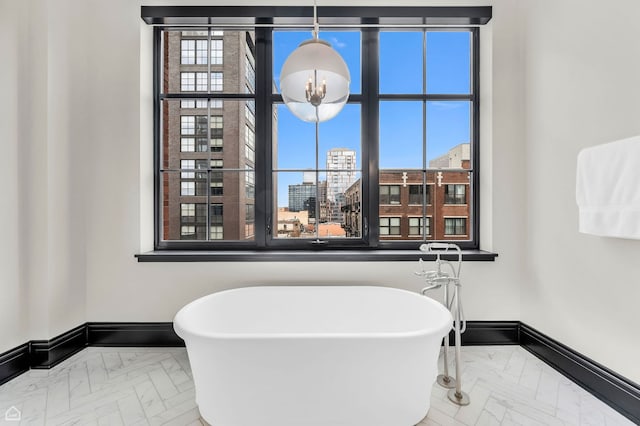full bath featuring an inviting chandelier, marble finish floor, baseboards, and a soaking tub