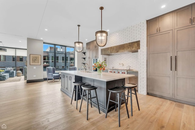 kitchen with pendant lighting, a breakfast bar, an island with sink, floor to ceiling windows, and light wood finished floors