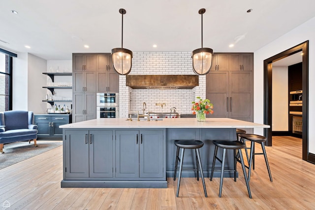 kitchen with tasteful backsplash, open shelves, light wood-type flooring, a sink, and light countertops