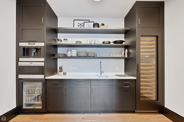 bar featuring light wood-style floors, a sink, wine cooler, and indoor wet bar