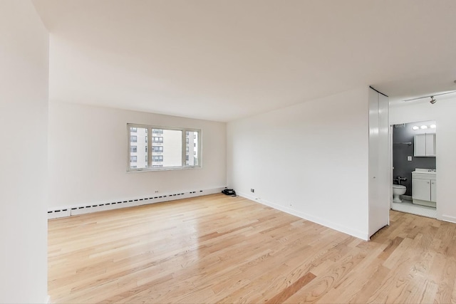spare room with baseboards, a baseboard heating unit, and light wood finished floors