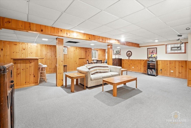 carpeted living area with wood walls, a bar, a drop ceiling, and plenty of natural light
