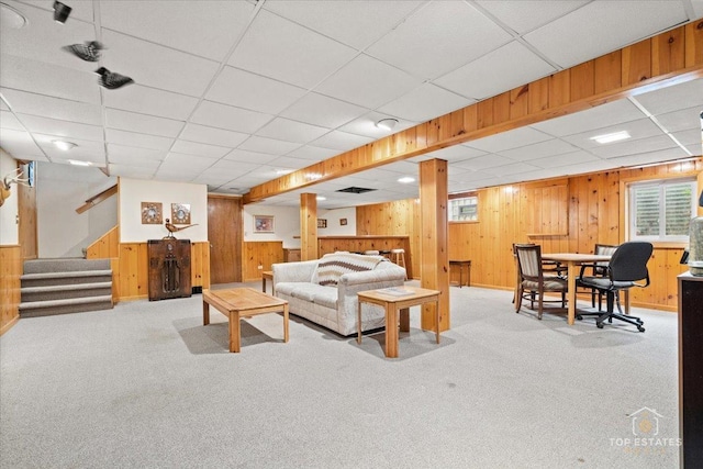 carpeted living area with stairway, wood walls, and a drop ceiling