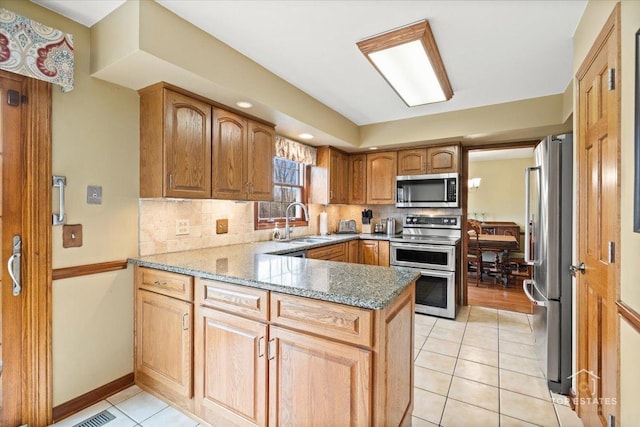 kitchen featuring a sink, light tile patterned floors, a peninsula, tasteful backsplash, and appliances with stainless steel finishes