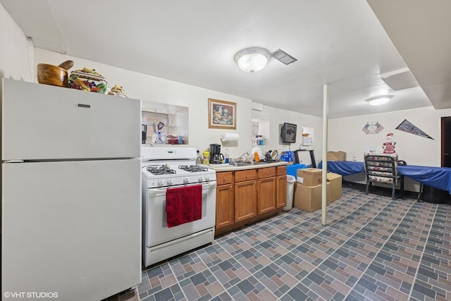 kitchen with a sink, white appliances, light countertops, brick patterned floor, and brown cabinetry