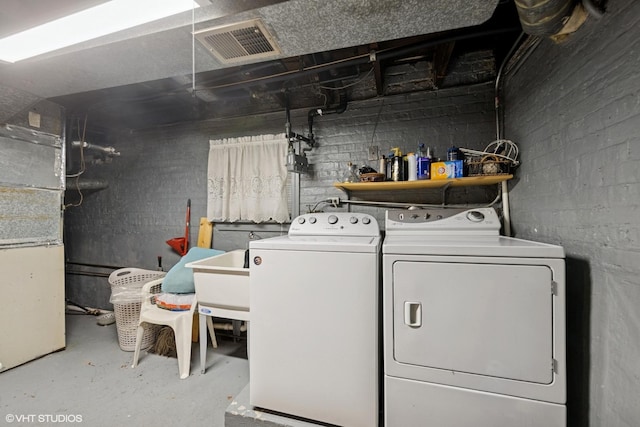 laundry room with laundry area, visible vents, washing machine and clothes dryer, a sink, and concrete block wall
