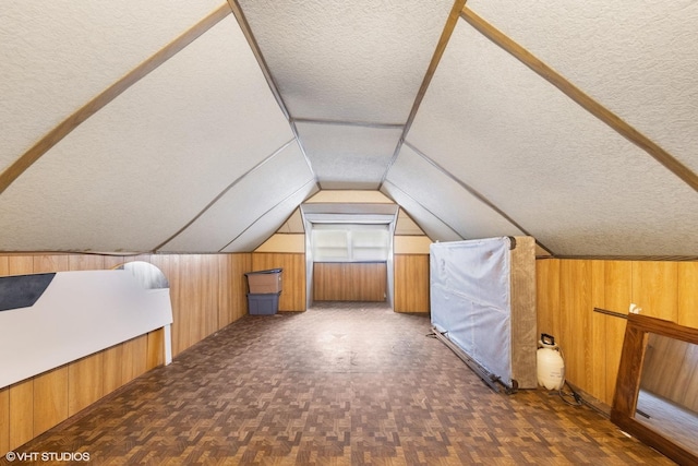 bonus room with vaulted ceiling, wood walls, and a textured ceiling