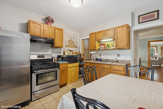 kitchen with decorative backsplash, appliances with stainless steel finishes, light countertops, light tile patterned floors, and under cabinet range hood