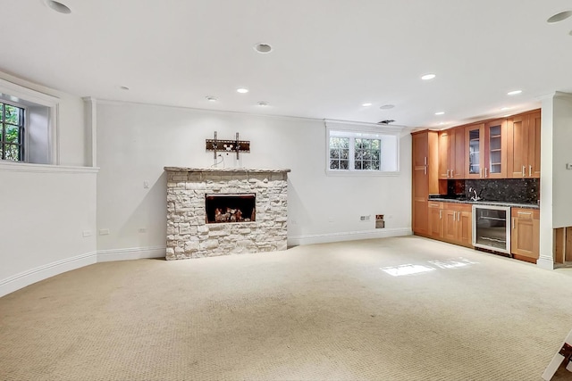 unfurnished living room featuring beverage cooler, light carpet, baseboards, recessed lighting, and a stone fireplace