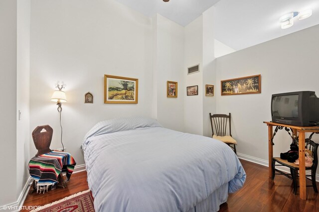 bedroom featuring dark wood finished floors, visible vents, baseboards, and a high ceiling