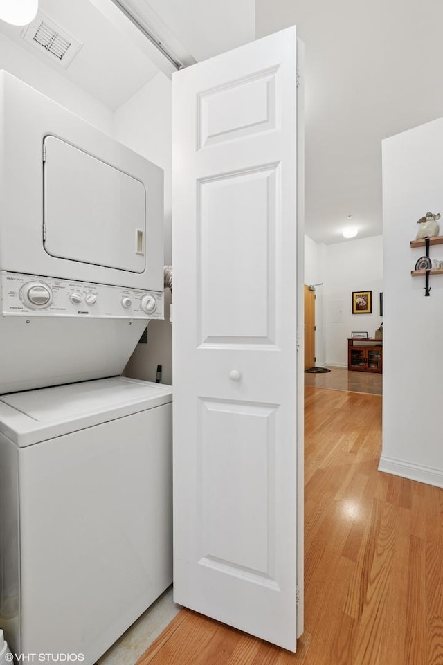 laundry room with stacked washer / dryer, laundry area, light wood finished floors, and visible vents