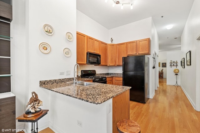 kitchen featuring light wood-style flooring, a sink, dark stone counters, brown cabinetry, and black appliances