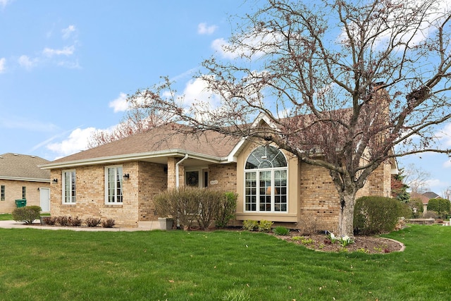 exterior space with a shingled roof, brick siding, and a front yard