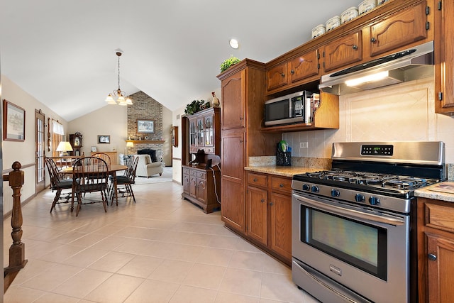 kitchen featuring tasteful backsplash, vaulted ceiling, under cabinet range hood, a fireplace, and appliances with stainless steel finishes