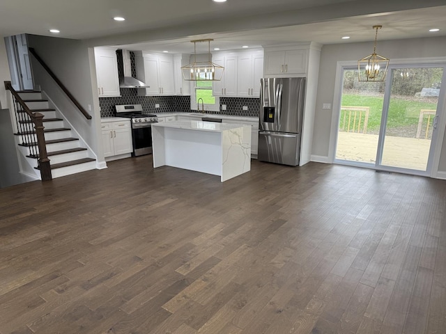 kitchen with wall chimney range hood, a chandelier, backsplash, appliances with stainless steel finishes, and a kitchen island