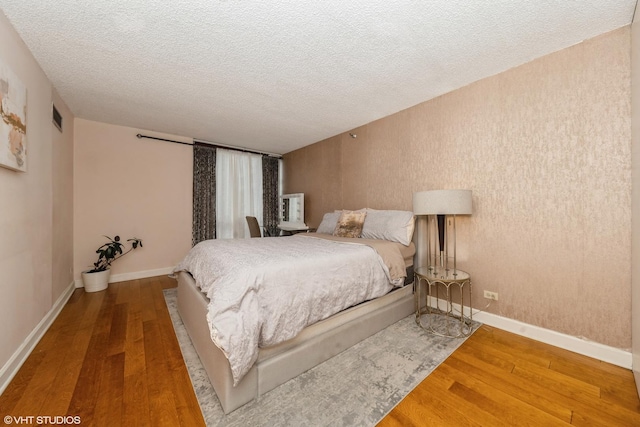 bedroom with visible vents, baseboards, a textured ceiling, and wood finished floors