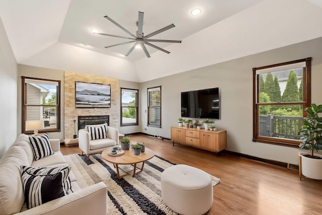 living area with ceiling fan, vaulted ceiling, light wood-type flooring, healthy amount of natural light, and a fireplace