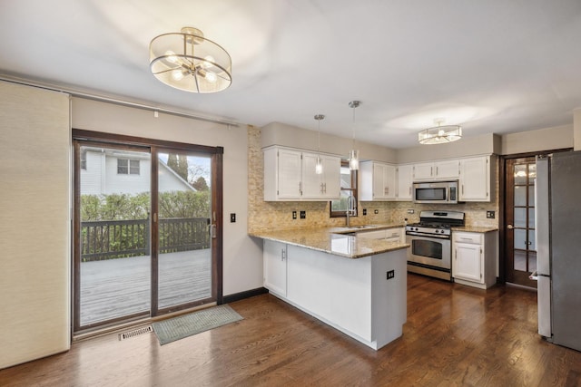 kitchen featuring appliances with stainless steel finishes, a chandelier, a peninsula, a sink, and decorative backsplash