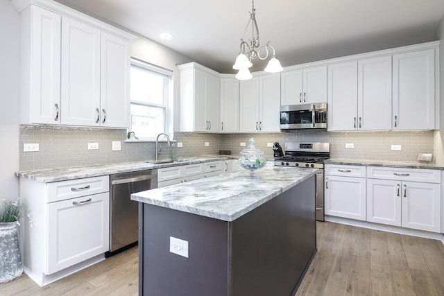 kitchen featuring white cabinets, appliances with stainless steel finishes, a sink, light wood-style flooring, and a center island