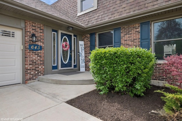 property entrance with brick siding, an attached garage, and roof with shingles