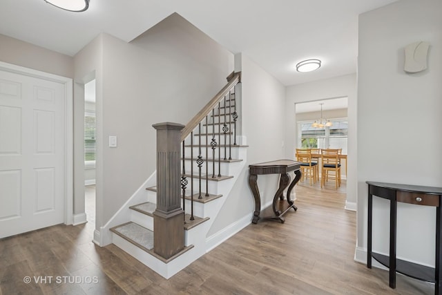 foyer entrance with baseboards, stairs, wood finished floors, and a chandelier