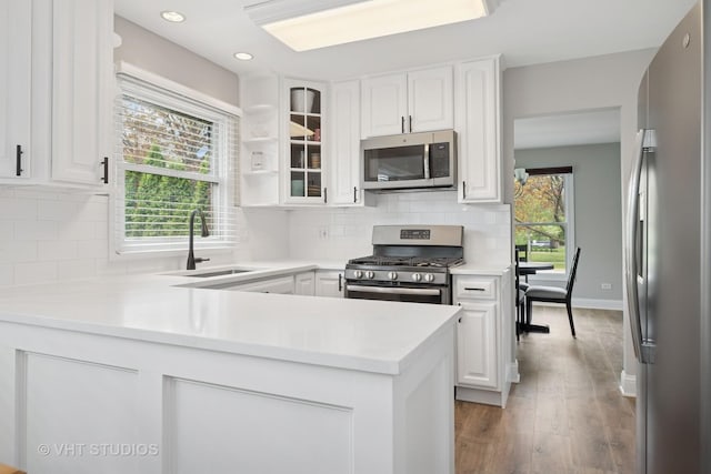 kitchen with a sink, white cabinetry, a peninsula, and stainless steel appliances