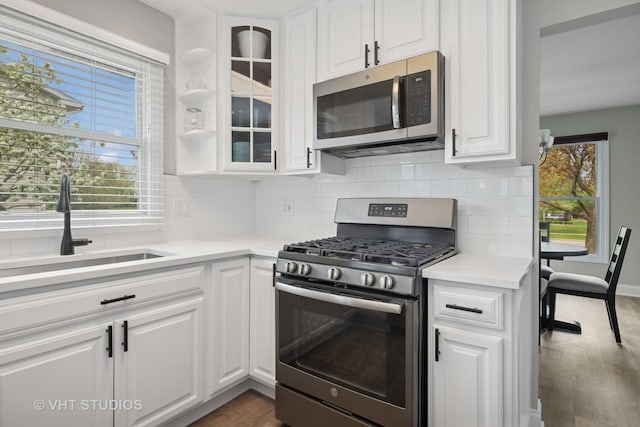 kitchen with backsplash, appliances with stainless steel finishes, wood finished floors, a sink, and white cabinetry