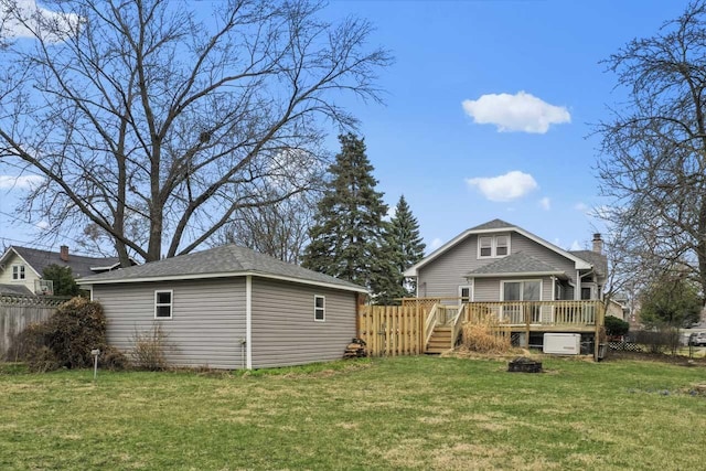 back of property with a yard, fence, a wooden deck, and an outbuilding