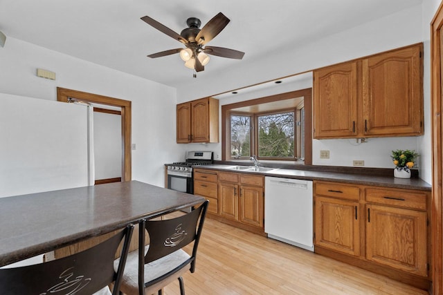 kitchen with stainless steel range with gas cooktop, brown cabinetry, light wood-style flooring, dishwasher, and a sink