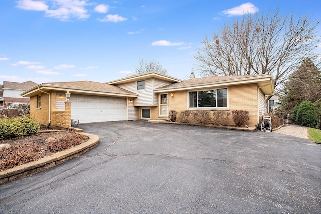 tri-level home featuring brick siding, fence, aphalt driveway, and a garage