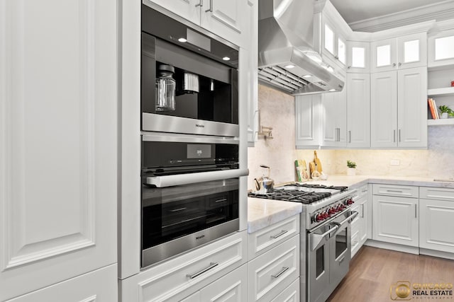 816 W Lill Ave, Chicago, IL 60614 - kitchen featuring wall chimney range hood, range with two ovens, light stone countertops, white cabinets, and ornamental molding