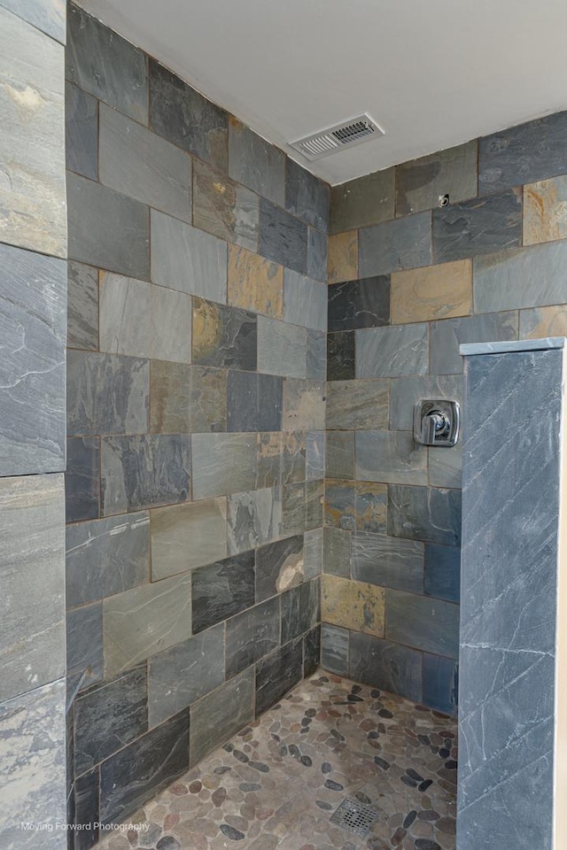 bathroom featuring tiled shower, stone finish floor, and visible vents
