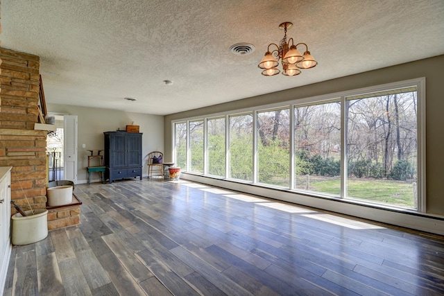unfurnished living room featuring wood finished floors, a textured ceiling, plenty of natural light, an inviting chandelier, and visible vents